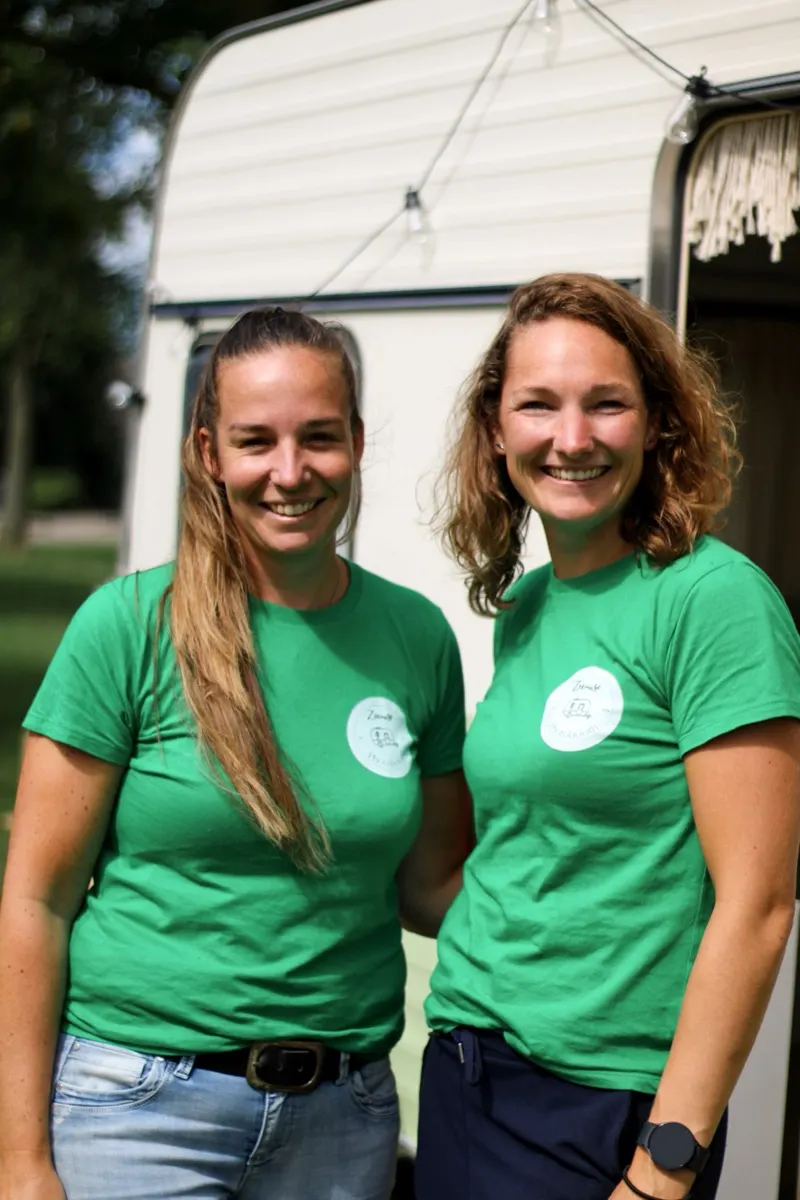 Chris (links) en Mariëlle (rechts) in groene Zeeuwse Photobooth-shirts, lachend voor de caravan